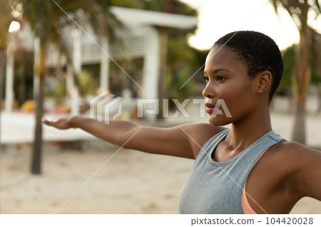 Focussed african american woman practicing yoga standing with arms outstretched on beach at sundown Focussed african american woman practicing yoga standing with arms outstretched on beach at sundown 104420028