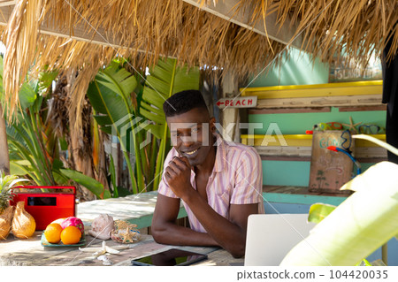 Portrait of happy african american man with laptop behind counter of surf hire beach shack Portrait of happy african american man with laptop behind counter of surf hire beach shack 104420035