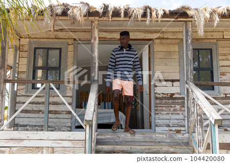 African american man walking down steps from porch of wooden beach house, looking away, copy space 104420080