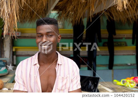 Portrait of happy african american man leaning on counter of surf hire beach shack, copy space Portrait of happy african american man leaning on counter of surf hire beach shack, copy space 104420152