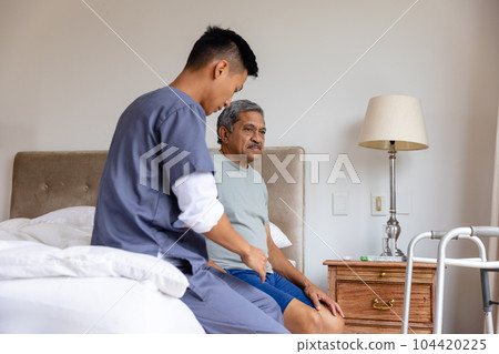 Diverse male doctor and senior male patient sitting on bed and discussing at home Diverse male doctor and senior male patient sitting on bed and discussing at home 104420225
