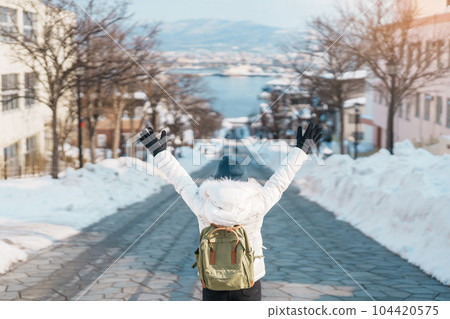 Woman tourist Visiting in Hakodate, Traveler in Sweater sightseeing Hachiman Zaka Slope with Snow in winter. landmark and popular for attractions in Hokkaido, Japan. Travel and Vacation concept 104420575