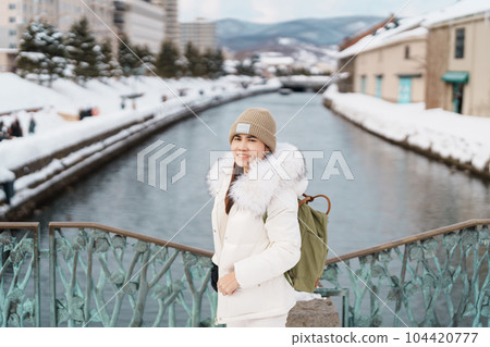 Woman tourist Visiting in Otaru, happy Traveler in Sweater sightseeing Otaru canal with Snow in winter season. landmark and popular for attractions in Hokkaido, Japan. Travel and Vacation concept 104420777