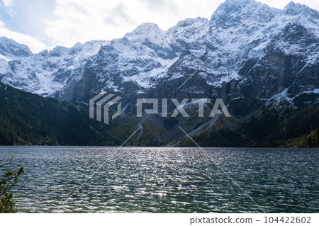Morskie Oko lake Snowy Mountain Hut in Polish Tatry mountains, Zakopane, Poland. Beautiful green hills and mountains in dark clouds and reflection on the lake Morskie Oko lake 104422602