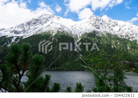 Morskie Oko lake Snowy Mountain Hut in Polish Tatry mountains, Zakopane, Poland. Beautiful green hills and mountains in dark clouds and reflection on the lake Morskie Oko lake 104422611