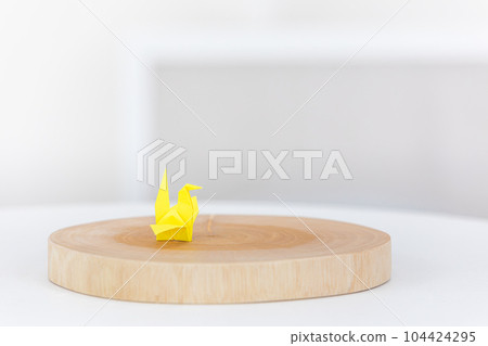 A single yellow paper crane on a wooden plate. 104424295