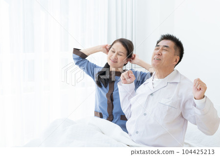 Smiling elderly couple stretching in bed in the morning Smiling elderly couple stretching in bed in the morning 104425213