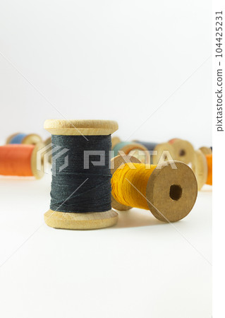 Wooden bobbins for black, yellow,  threads on white isolated background. Handmade, needlework, sewing items. Copy space 104425231
