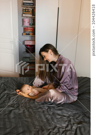 Happy mother holds a baby baby in her arms, smiling, sitting on the bed 104426418