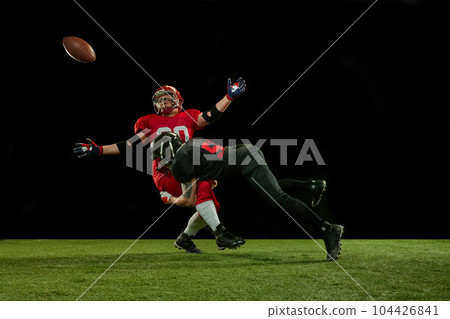 Defender. Two men, american football players in full uniform and equipment on field playing over black background 104426841