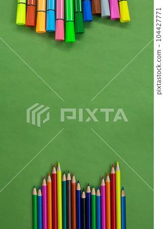 Colored felt tip pens and pencils in a row at the bottom and top or side with empty space for text on green. Back to school concept, drawing. Copy space 104427771