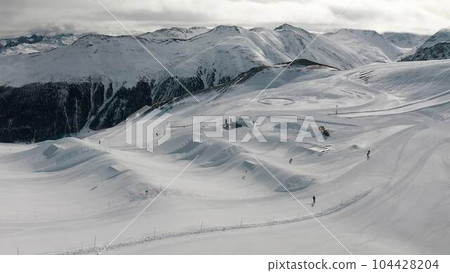 Livigno, Italy - February 21, 2022: People snowboarding and skiing at ski resort. Skiers and snowboarders riding snowy mountain slope. Outdoor winter sport. Aerial footage Livigno, Italy - February 21, 2022: People snowboarding and skiing at ski resort. Skiers and snowboarders riding snowy mountain slope. Outdoor winter sport. Aerial footage 104428204