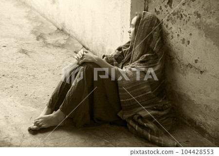 A girl in poor clothes sits on the ground 104428553