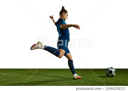 Young sportive girl in blue uniform, football player in motion, training, kicking ball against white background 104429223