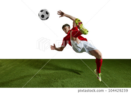 Champion. Young man, professional football player in motion, kicking ball in jump and falling on field against white background 104429239