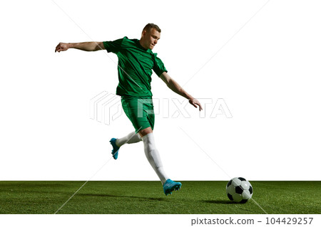 Young man in green uniform, football in motion, playing, kicking ball on sports field against white background 104429257