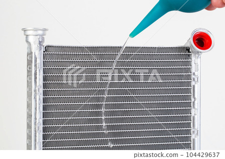 A jet of water from a syringe pours onto a car radiator. The concept of cleaning and flushing car radiators from pollution. Clogged radiator cells. A jet of water from a syringe pours onto a car radiator. The concept of cleaning and flushing car radiators from pollution. Clogged radiator cells. 104429637
