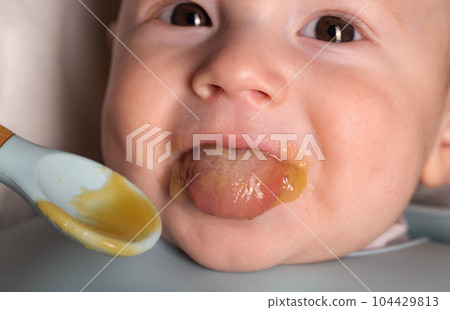 A small child of 5 months tries vegetable puree for the first time in his life, close-up 104429813