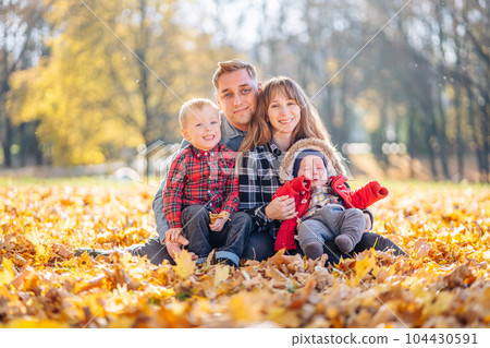 A young family sits in the park on a leafy, sunny autumn day. A young family sits in the park on a leafy, sunny autumn day. 104430591