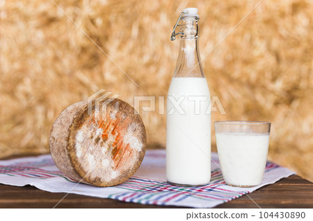 bottle and glass of milk and a head of cheese on table in barn against background of hay bottle and glass of milk and a head of cheese on table in barn against background of hay 104430890