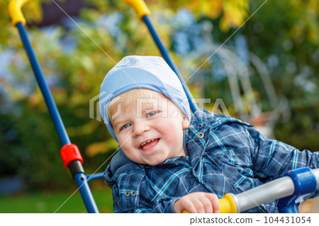 Cute little boy playing with tricycle bike outdoors. Happy child play in autumn park. Toddler baby boy wears trendy jacket. smiling Blonde boy portrait. Autumn fashion. Stylish child outside. 104431054