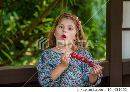Little girl eating delicious strawberries on skewers, savoring the simple pleasures of family and healthy food. Happy preschool child eat fresh berries 104431062