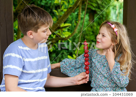 A joyful moment as a little girl and a teenager boy share delicious strawberries on skewers, savoring the simple pleasures of family and healthy food. Happy Family eat fresh berries A joyful moment as a little girl and a teenager boy share delicious strawberries on skewers, savoring the simple pleasures of family and healthy food. Happy Family eat fresh berries 104431069