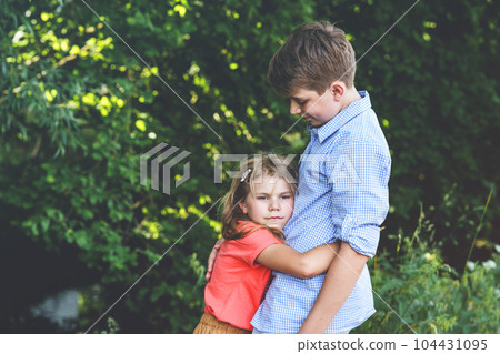 An upset little girl finds comfort in the embrace of her caring teenage brother, exemplifying the bond of a loving family. Loving Siblings, Brother and Sister. 104431095