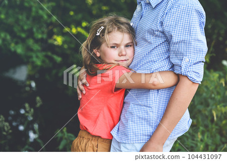 An upset little girl finds comfort in the embrace of her caring teenage brother, exemplifying the bond of a loving family. Loving Siblings, Brother and Sister. 104431097