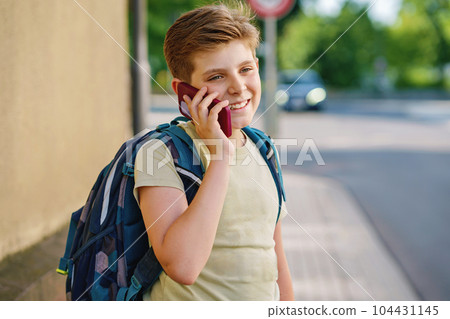 Handsome teenager boy speaking on the smartphone. Preteen child with mobile cell phone on the street on the way to school. Handsome teenager boy speaking on the smartphone. Preteen child with mobile cell phone on the street on the way to school. 104431145