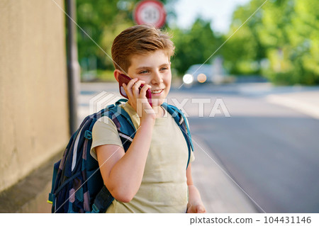 Handsome teenager boy speaking on the smartphone. Preteen child with mobile cell phone on the street on the way to school. Handsome teenager boy speaking on the smartphone. Preteen child with mobile cell phone on the street on the way to school. 104431146