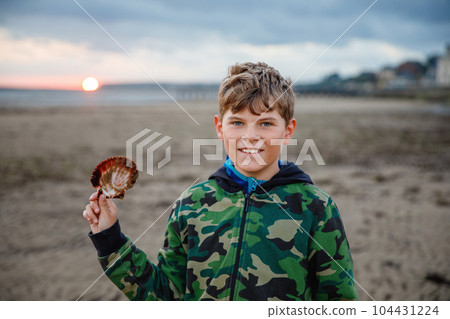 School Boy Plays on a Norman Beach in Normandy, Embracing the Joy of Sandy Shores, Seashells, and Carefree Exploration. Happy Child and Family Vacation in France. School Boy Plays on a Norman Beach in Normandy, Embracing the Joy of Sandy Shores, Seashells, and Carefree Exploration. Happy Child and Family Vacation in France. 104431224