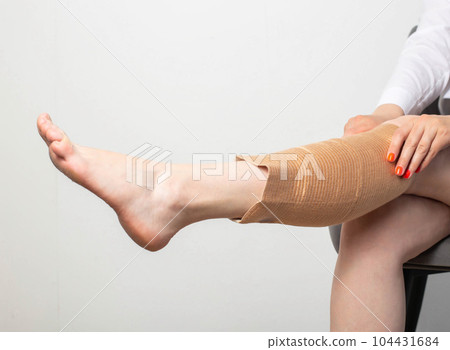 The girl puts on an elastic orthopedic knee pad on a sore leg. Arthrosis and knee injury. Fixation of the knee joint. Copy space for text The girl puts on an elastic orthopedic knee pad on a sore leg. Arthrosis and knee injury. Fixation of the knee joint. Copy space for text 104431684