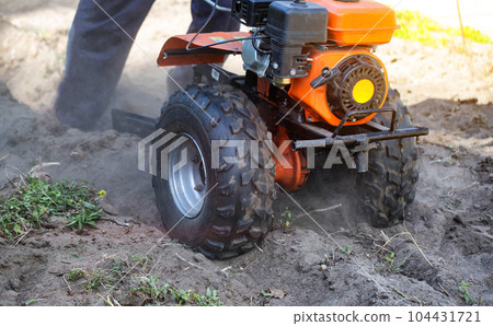 Plowing a garden with potatoes with a walk-behind tractor. Harvesting potatoes in autumn. Plowing the furrow with a motor-block with a plow. Industry 104431721