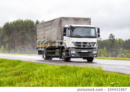 A tilt truck transports cargo on a highway in rainy weather on a slippery road. The concept of import substitution. Copy space for text A tilt truck transports cargo on a highway in rainy weather on a slippery road. The concept of import substitution. Copy space for text 104431967