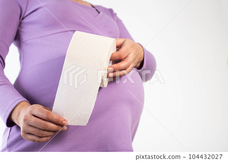 A pregnant girl in a lilac blouse holds toilet paper against the background of her belly. The concept of constipation in pregnant women. Copy space for text A pregnant girl in a lilac blouse holds toilet paper against the background of her belly. The concept of constipation in pregnant women. Copy space for text 104432027