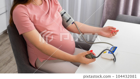 A pregnant girl measures blood pressure with a device. The concept of high and low blood pressure during pregnancy. Arterial hypertension. Copy space for text A pregnant girl measures blood pressure with a device. The concept of high and low blood pressure during pregnancy. Arterial hypertension. Copy space for text 104432081