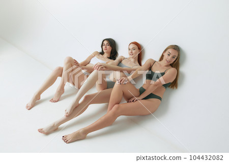 Relaxed. Beautiful redhead, brunette and blonde young women with slim body posing in underwear against grey studio background Relaxed. Beautiful redhead, brunette and blonde young women with slim body posing in underwear against grey studio background 104432082