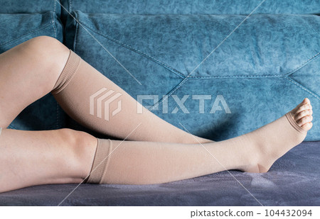 Girl's legs in compression stockings for varicose veins. Pregnancy and varicose veins Legs of a girl at home on the sofa. Pain and swelling in the legs. 104432094