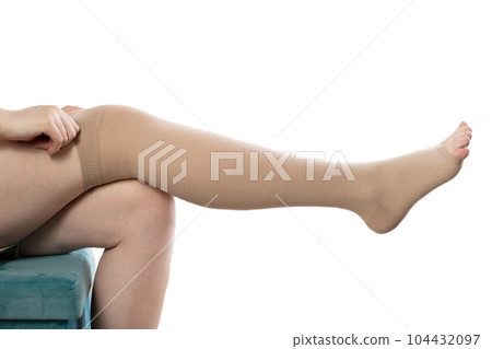 Pregnant girl puts on compression stockings for varicose veins on her legs. White background. Pregnancy and varicose veins, phlebology. 104432097