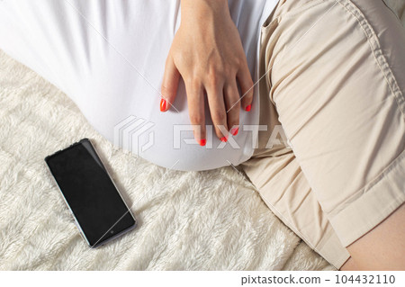 A pregnant girl holds a mobile phone near her belly. The concept of harm and deviations in the development of the unborn child. The negative impact of cellular radiation on pregnant women. 104432110