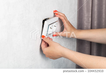 The girl is trying to insert a torn out socket from the socket due to the wrong pulling out of the electrical plug. Close-up, girl's hands with manicure. 104432910