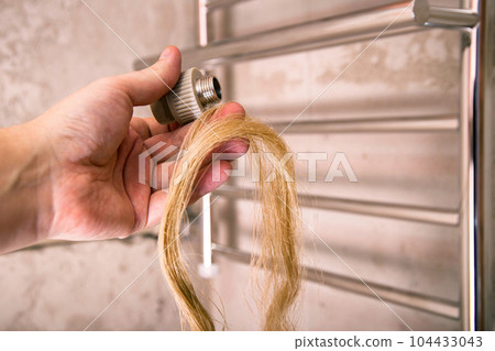 Fitting and sanitary flax in hand against the background of a heated towel rail. The concept of using linen in plumbing against water leaks. Close-up 104433043
