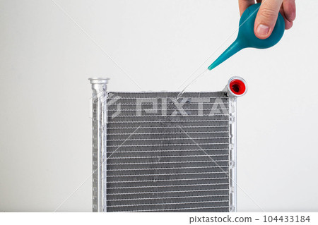 A jet of water from a syringe pours onto a car radiator. The concept of cleaning and flushing car radiators from pollution. Clogged radiator cells. Copy space for text 104433184