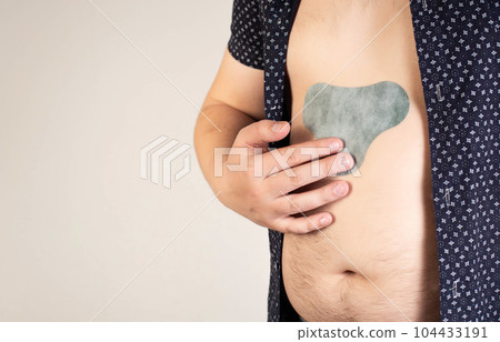 A man in a black shirt sticks an anesthetic patch on his stomach. Relieve pain and tension. Copy space for text A man in a black shirt sticks an anesthetic patch on his stomach. Relieve pain and tension. Copy space for text 104433191