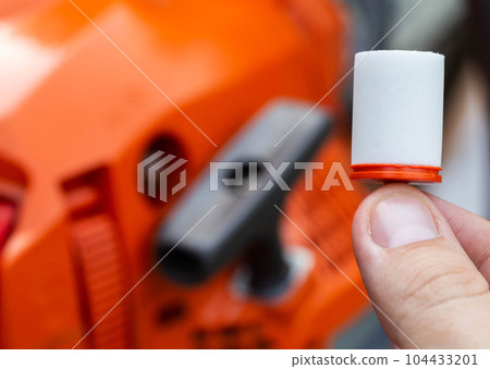 New fuel filter on the background of a chainsaw. The concept of replacing the fuel filter and protecting the engine from impurities, water and dirt in the fuel. Close-up 104433201