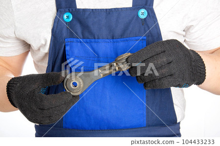 A car mechanic holds in his hands a part of a car suspension, a stabilizer link. Repair and replacement of car auto parts at a car service, close-up A car mechanic holds in his hands a part of a car suspension, a stabilizer link. Repair and replacement of car auto parts at a car service, close-up 104433233