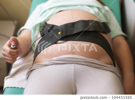A pregnant woman undergoes a medical examination. Cardiotocography for an infant. A method of functional assessment of the state of the fetus during pregnancy and childbirth, which allows you to see A pregnant woman undergoes a medical examination. Cardiotocography for an infant. A method of functional assessment of the state of the fetus during pregnancy and childbirth, which allows you to see 104433388