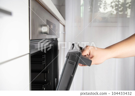 A man opens a modern oven door with child protection function. Oven with pizza mode function and 3d hot air 104433432