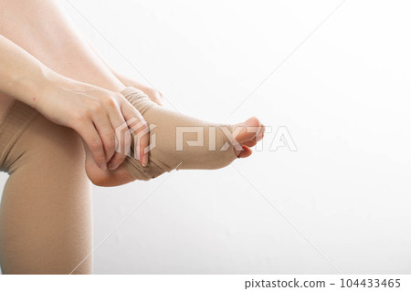 Pregnant girl puts on compression stockings for varicose veins on her legs. White background. Pregnancy and varicose veins, phlebology. Pregnant girl puts on compression stockings for varicose veins on her legs. White background. Pregnancy and varicose veins, phlebology. 104433465